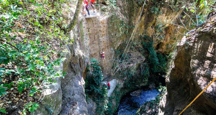 Abenteuerlustige beim Klettern und Abseilen an den steilen Wänden einer engen Dschungelschlucht mit einem Bach darunter.