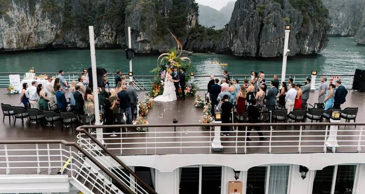 Wedding ceremony takes place on a ship deck surrounded by guests and emerald karst formations