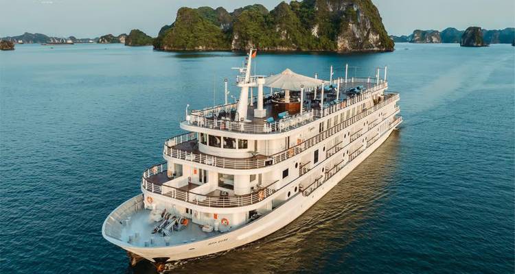 Aerial view of a multi-deck white cruise ship gliding across blue waters near forested islets