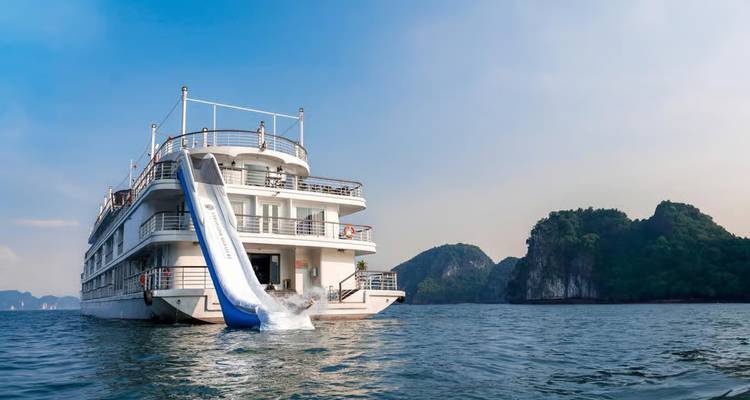 Cruise ship with a giant inflatable slide splashes into the sea against a backdrop of green cliffs