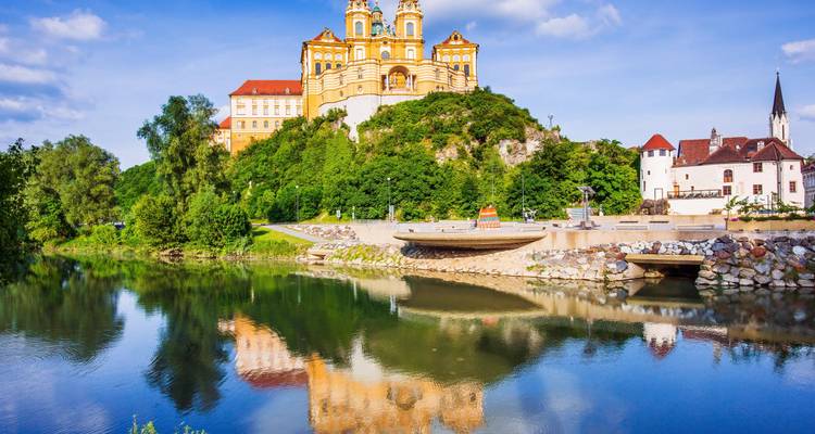 De gele barokgebouwen van Melk Abbey kronen een bosrijke heuvel met uitzicht op de glinsterende Donau.
