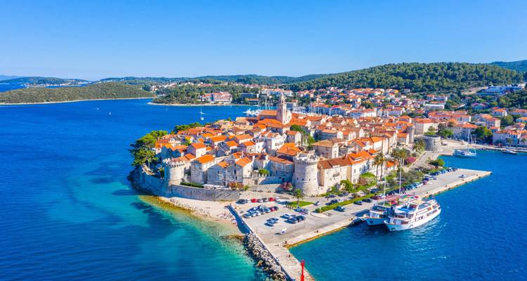 Luftaufnahme einer mittelalterlichen ummauerten Stadt mit orangefarbenen Dächern auf einer Halbinsel, umgeben von der türkisfarbenen Adria.