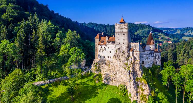 El Castillo de Bran encaramado en una colina rocosa y boscosa bajo un cielo azul despejado en Rumania.