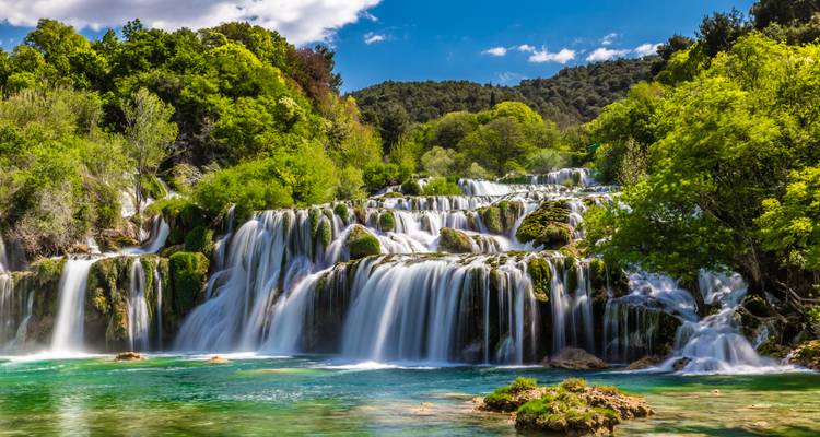 Multiple tiers of emerald waterfalls cascade into clear turquoise pools at Krka National Park.