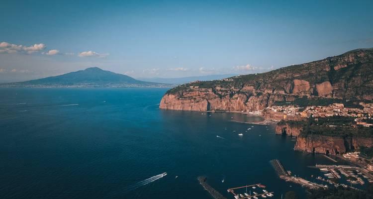Wide coastal panorama of the Bay of Naples with Sorrento cliffs and Mount Vesuvius on the horizon.