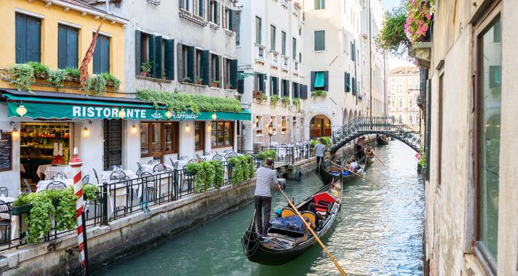 Les gondoliers naviguent dans un étroit canal vénitien devant un ristorante accueillant aux fenêtres ornées de fleurs.