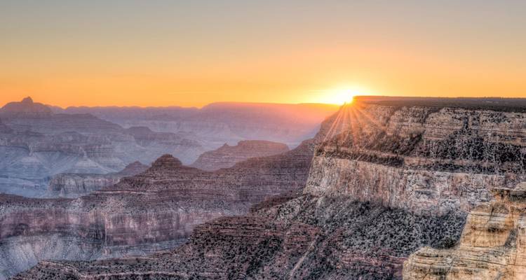 Lever de soleil doré projetant ses rayons sur les falaises en couches du Grand Canyon.