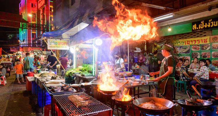 Lebhafter Bangkoker Nachtmarkt mit flammenden Woks, Straßenverkaufsständen und Neonlichtern.