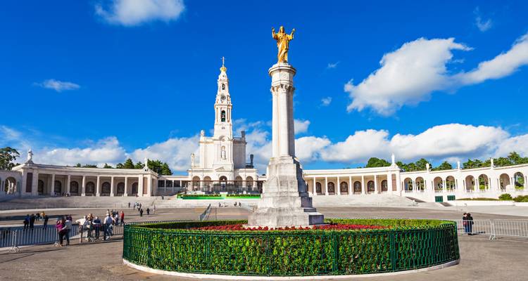 Plaza amplia del Santuario de Fátima con una columna alta y basílica recortada contra un cielo azul brillante.