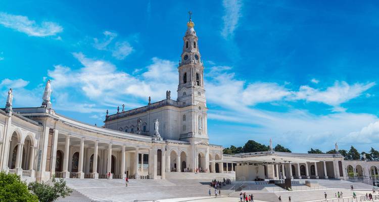 Vista lateral de la basílica de Fátima y sus amplios colonnados mientras visitantes pasean por el espacioso atrio.