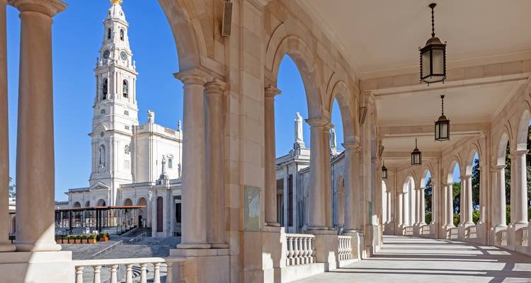 Arcada de mármol enmarcando una vista distante de la basílica de Fátima bajo cielos azules despejados.
