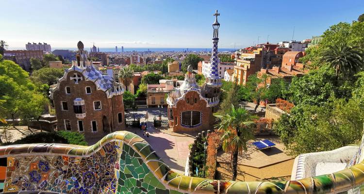 Terraza de mosaico colorido del Parque Güell con vistas al paisaje urbano de Barcelona y al mar Mediterráneo en un día despejado.