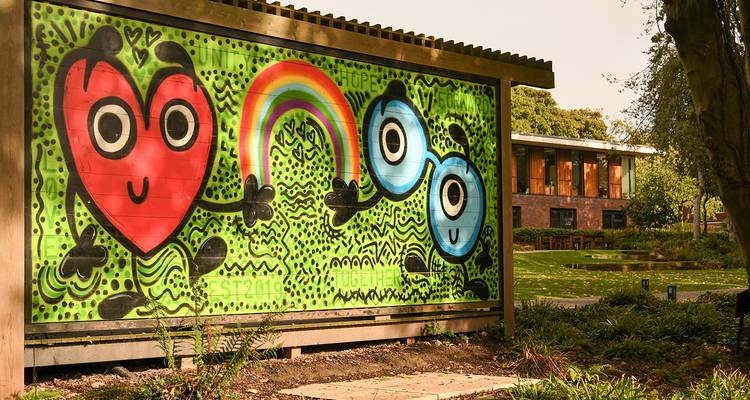 Fresque murale de street-art brillante et ludique représentant des personnages de bande dessinée avec un arc-en-ciel, situé dans un cadre de parc verdoyant.