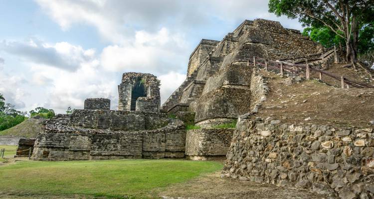Ruines de pierre d'un complexe de temples Maya anciens se dressant contre un ciel partiellement nuageux et une pelouse verdoyante.