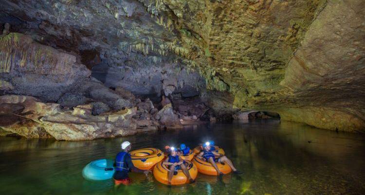 Les aventuriers dans des tubes gonflables portant des lampes frontales flottent à travers une rivière souterraine dramatique remplie de stalactites.