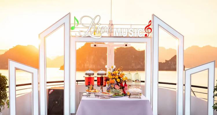Elegante zona en la azotea de un crucero con snacks de bufé, dispensadores de bebidas y un letrero de 'Música en Vivo' con islas de piedra caliza al fondo.