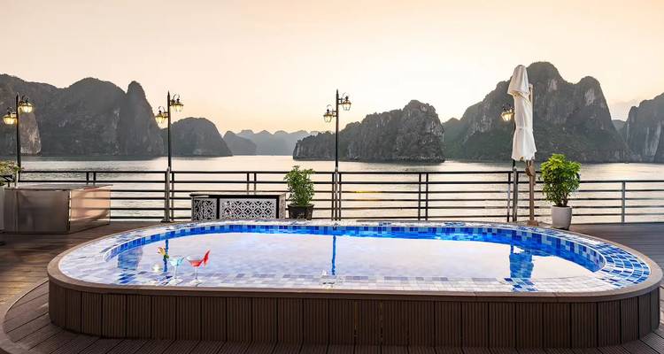 Pequeña piscina ovalada en la cubierta de un crucero que refleja el cielo, con los pilares de piedra caliza de la Bahía de Ha Long de fondo al atardecer.