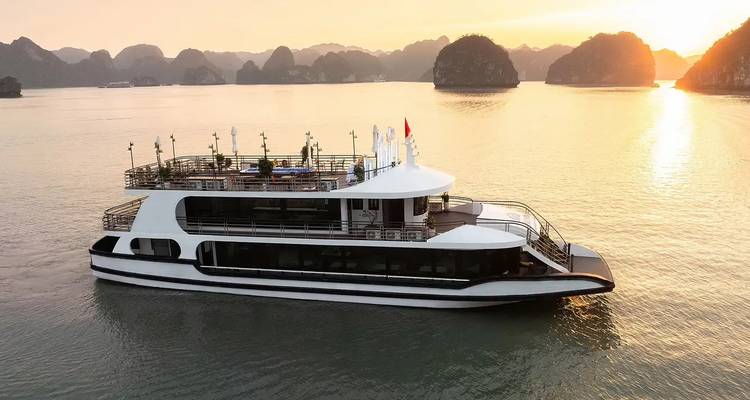 Moderno crucero de día blanco en aguas doradas con el paisaje de piedra caliza de la Bahía de Ha Long recortado por el sol poniente.