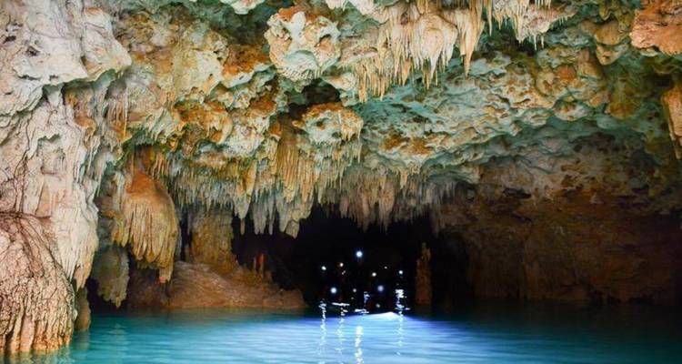 Grotte calcaire illuminée avec des stalactites spectaculaires au-dessus d'une eau turquoise