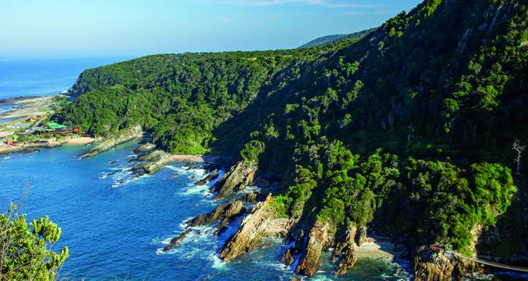 Üppig bewaldete Klippen, die an der rauen Küste der Garden Route steil ins tiefe blaue Meer abfallen.