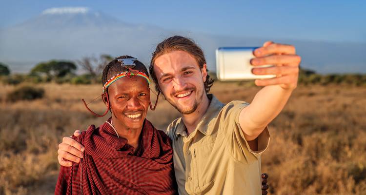 Un voyageur et un habitant Maasai prennent un selfie joyeux avec le Mont Kilimandjaro qui se dresse majestueusement dans l'arrière-plan brumeux.