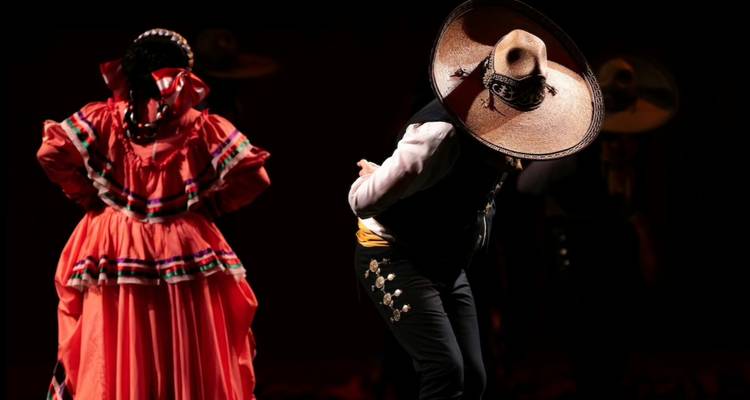 Folkloristische Tanzaufführung mit einem Charro-Musiker und einer Frau in leuchtend rotem traditionellem Kleid auf der Bühne