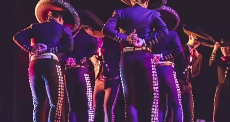 Gruppe von Mariachi-Musikern in dunkler Kleidung und Sombreros, die auf der Bühne in Formation stehen