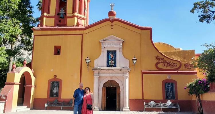 Couple standing in front of a small yellow colonial church under a clear blue sky