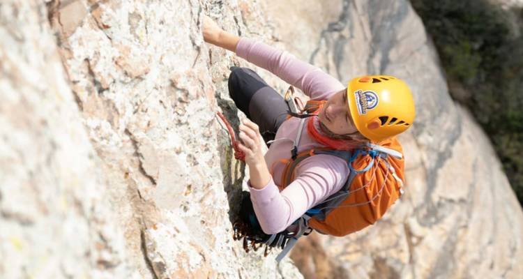Rock climber wearing helmet and backpack scaling a steep granite wall
