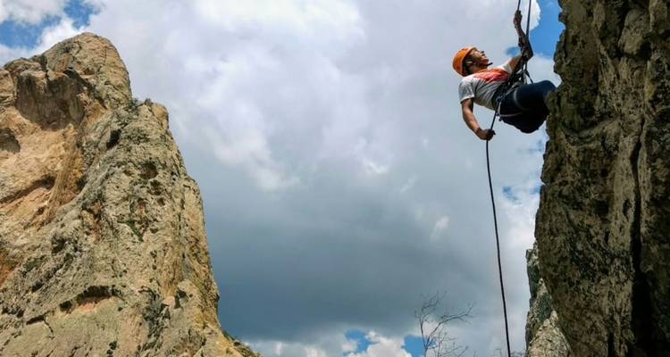 Rappelling climber descending a rocky cliff against a backdrop of blue sky and clouds