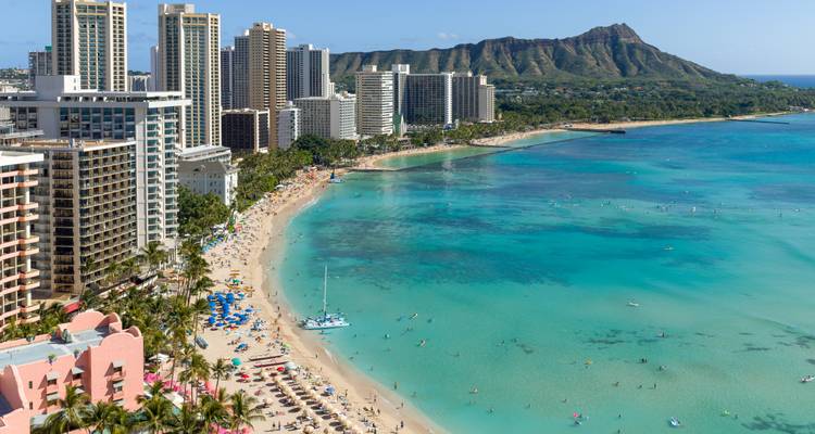 Vista aérea de la costa curva de Waikiki con aguas turquesas y el cráter Diamond Head a lo lejos.