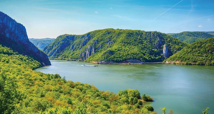 Uitgebreid uitzicht op de Ijzeren Poort kloof van de Donau met beboste rotsen en een vrachtschip onder een strakblauwe hemel.
