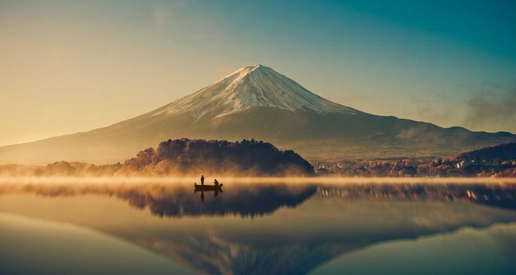 El Monte Fuji con sus cimas nevadas se refleja perfectamente en el neblinoso Lago Kawaguchiko al amanecer con una pequeña barca.