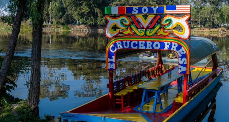Buntes Trajinera-Boot, gespiegelt in den ruhigen Kanalgewässern von Xochimilco, mit lebendigen Schildern dekoriert
