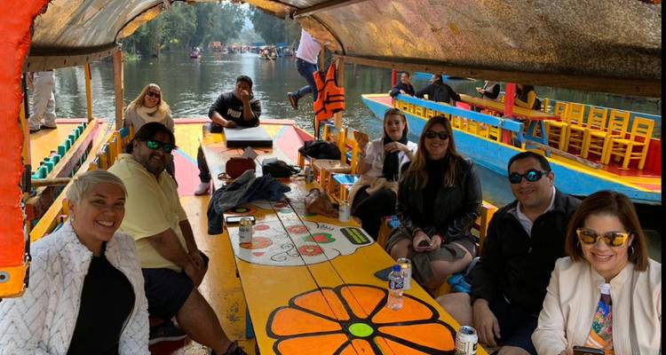 Gruppe von Freunden, die eine farbenfrohe Bootsfahrt auf den Xochimilco-Kanälen um einen bemalten Holztisch sitzend genießt
