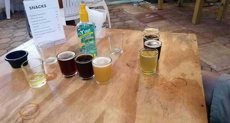 Holztisch mit verschiedenen Bierproben und einer Flasche Handdesinfektionsmittel in einem offenen Innenhof.