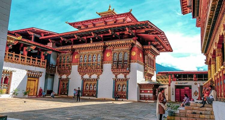 Cour colorée de dzong bhoutanais avec boiseries ornementales alors que les visiteurs explorent le site.