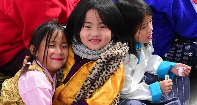 Trois enfants bhoutanais vêtus de vêtements traditionnels souriant chaleureusement à la caméra.
