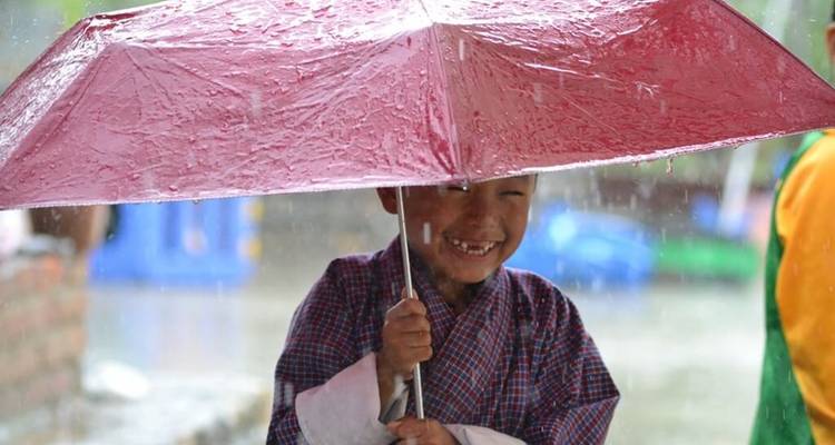 Un enfant qui rit, abrité sous un parapluie rose mouillé lors d'une averse.