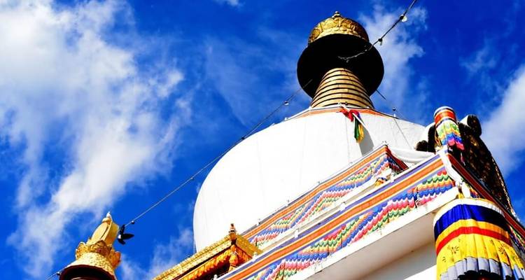 Stupa bhoutanais blanc surmonté d'un pinacle doré encadré par un ciel bleu éclatant et des drapeaux de prière.