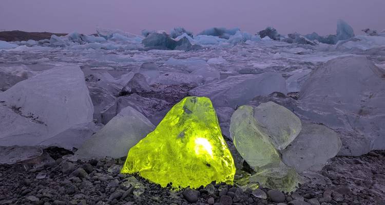 Luminescent gele ijsblok die oplicht tussen verspreid liggende ijsbergen op een bevroren kust