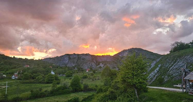 Dramatischer Sonnenuntergang, der ein orangefarbenes Glühen über felsige Hügel und verstreute Dorfhäuser wirft
