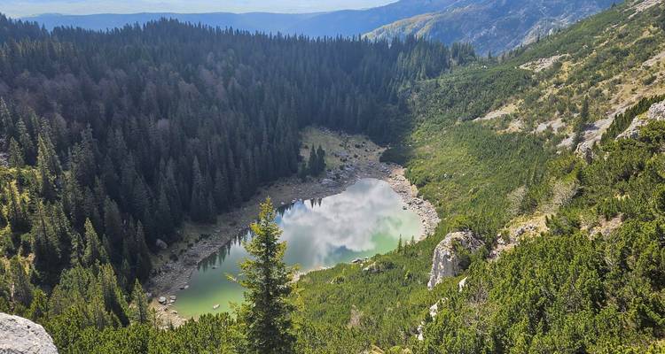 Kleiner herzförmiger Alpensee, umgeben von Nadelwald, von einem hohen Bergrücken aus betrachtet