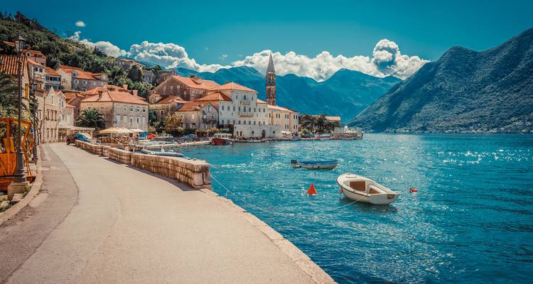 Malerisches adriatisches Küstendorf mit steinerner Uferpromenade und Booten, die auf türkisfarbenem Wasser schwimmen