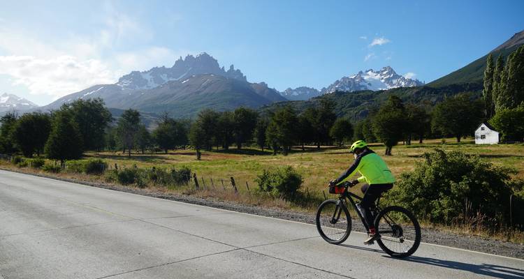 Road cyclist passing scenic jagged peaks and meadows on a sunny day in Patagonia