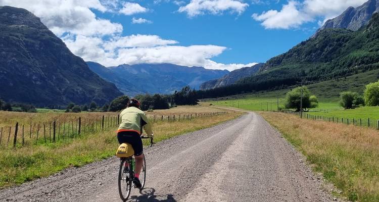 Cyclist pedalling along a gravel road between lush valleys and towering Patagonian peaks