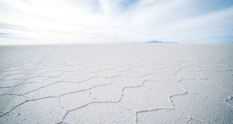 Endless white salt flat with polygon patterns stretching to the horizon under a pale blue sky.