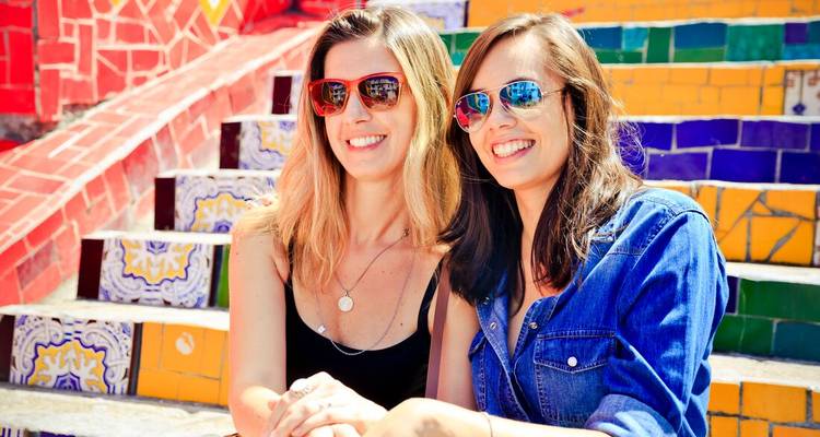 Two smiling women wearing colourful sunglasses sit on Rio’s mosaic Selarón Steps.