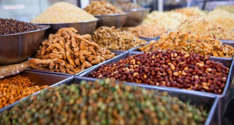 Assortiment de bols remplis de lentilles colorées, de noix et de collations exposés à un étal de marché indien.