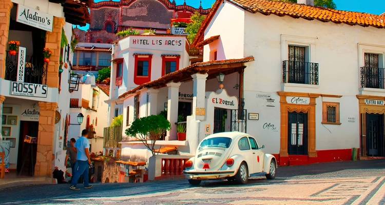 Pintoresca calle colonial en Taxco con fachadas coloridas y un clásico Volkswagen Beetle blanco.